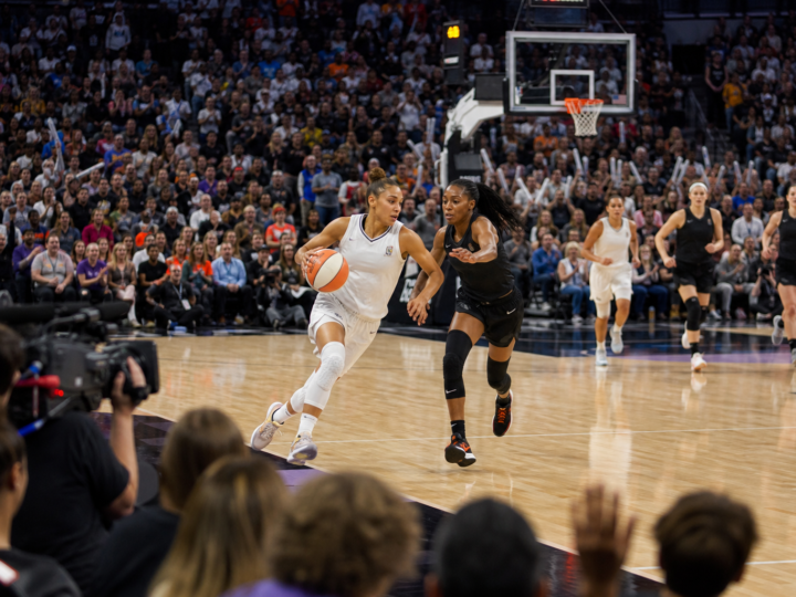 Women’s basketball players competing in a bright packed arena as fans cheer.
